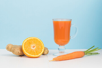Ginger, half an orange, carrots and a glass glass with a smoothie on a white table.