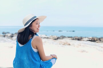Asian traveler woman sitting and relaxing at the beach by the sea background.Concept of happy travel on vacation weekend.