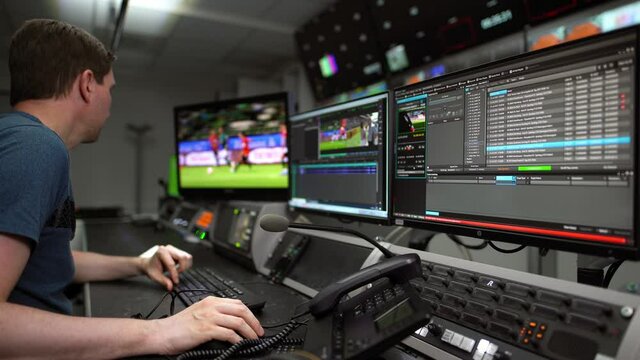 Man at work in a TV company - cutting a sport video sitting on a table in front of some monitors and communication elements like a intercom and a telephone.