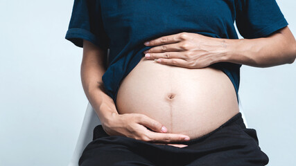 Asian pregnant woman hugging her belly with love for her unborn baby. Close-up shot.