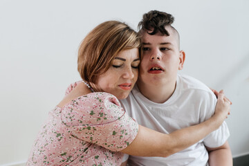 Mother hugging disabled boy 17 years old in wheelchair with cerebral palsy over white background. Woman assists person with Special Needs. Emotional family lives with disability, holding hands