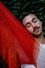 young latin hispanic man with his head lying on a red sarong, model posing. artistic photo. vertical