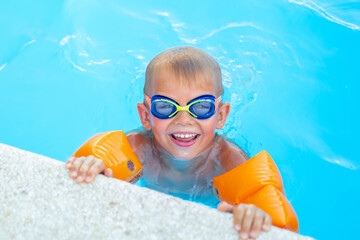 Portrait smiling boy in swimming pool, child in swimming glasses and inflatable sleeves. Summer travel hotel vacation or classes