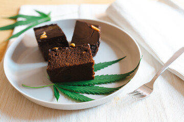 Homemade sweetmeat with marijuana or cannabis leaf on white plate. Alternative medicine concept..