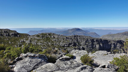 Fototapeta na wymiar On the top of Table Mountain in Cape Town, there are fynbos bushes. Cracks on gray spotted boulders. Clear blue sky and clouds on the horizon. South Africa