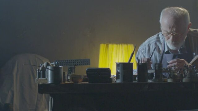 Footage of goldsmith working at table in workshop . Bearded old man jeweler creating new jewelry . Master goldsmith working process . Scenic film shot in vintage style. Shot on RED EPIC Camera.   