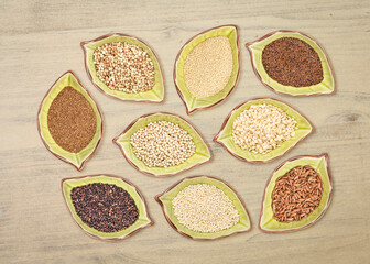 nine gluten free grains (black quinoa, buckwheat, amaranth, teff, sorghum, kaniwa, millet, and brown rice) - top view of leaf shaped ceramic bowls against distressed wood