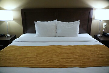 A comfortable bed with white pillows, bed sheet and mustard blanket