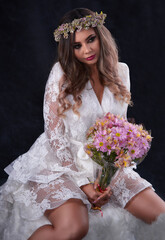 Young bride with bouquet of flowers sitting isolated on black