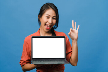 Young Asia lady show empty laptop screen with positive expression, smiles broadly, dressed in casual clothing feeling happiness isolated on blue background. Computer with white screen in female hand.