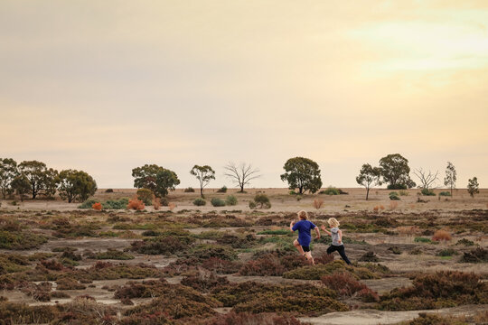 Brothers running while exploring desolate dry lake together. Family outing in the Australian bush.
