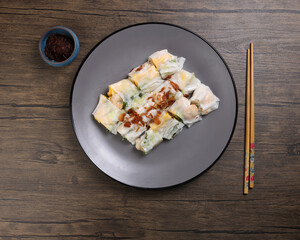 Chinse steamed rice noodle roll cheung fun stuffed shrimp prawn chicken vegetable fried onion garnish on dark plate sauce chopsticks on rustic dark wood table