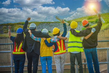Group of engineer show hand up to cheer up with group at construction site while holding a...