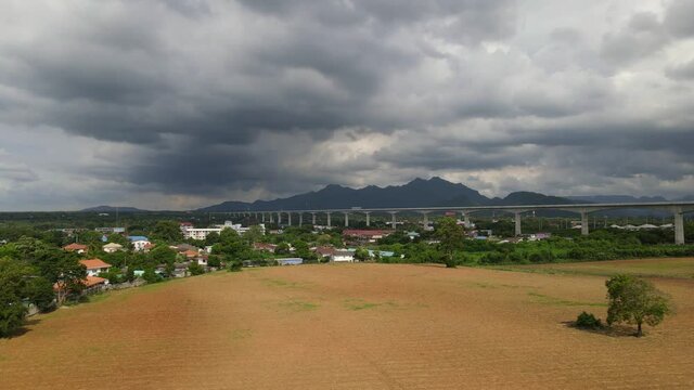Aerial footage of a landscape and agricultural fertile land, newly built elevated railway across town in countryside of Saraburi in Thailand during a cloudy day in the afternoon.