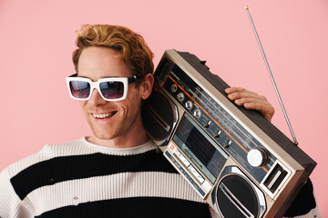 Ginger young man wearing sunglasses posing with retro tape recorder