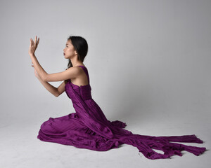 Full length  portrait of pretty brunette asian girl wearing purple flowing  gown. Sitting pose on...