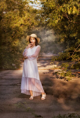 A young girl in a park in a white dress and a hat