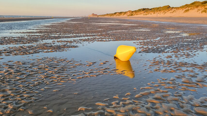 Scenic coast of the  sea during low tide, dunes at background at the sunset. Yellow buoy in front.