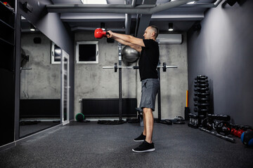 Fototapeta na wymiar Proper posture of the body and arms exercising, sports discipline. An attractive man with both hands raised a kettle bell with both hands in the line with his shoulders in the gym
