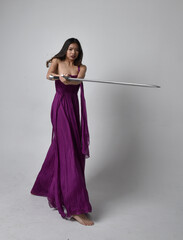 Full length  portrait of pretty brunette asian girl wearing purple flowing  gown. Sitting pose...