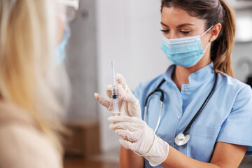Nurse with face mask and rubber gloves holding vaccine and preparing it for injection.