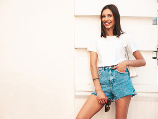 Portrait of young beautiful smiling hipster woman in trendy summer jeans shorts. Sexy carefree model posing on the street background at sunset. Positive model outdoors in sunglasses