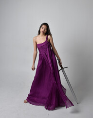 Full length  portrait of pretty brunette asian girl wearing purple flowing  gown. Sitting pose...