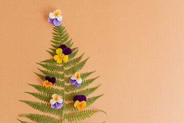 Naklejka premium christmas tree made of fern leaves and pansies on beige background with copy space. New year concept
