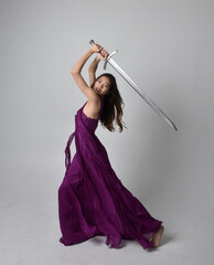 Full length  portrait of pretty brunette asian girl wearing purple flowing  gown. Sitting pose...