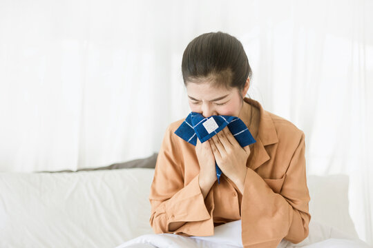 Young asian woman  sneezing and blowing her nose with .handkerchief on her bed. Allergy symptom  or flu or cold.