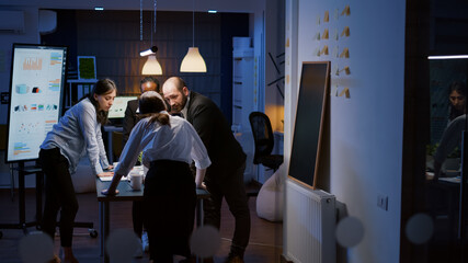 Multi ethnic businesspeople teamwork standing at conference table analyzing management graphs in...