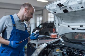 Mechanic checking a car's oil level in the garage - obrazy, fototapety, plakaty