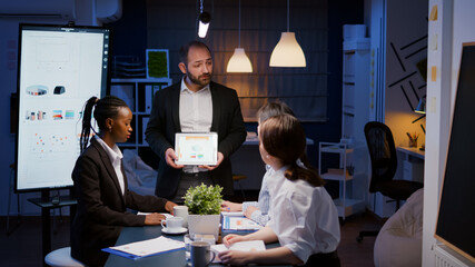 Focused workaholic entrepreneur man working overtime presenting company statistics using tablet....