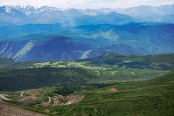 Fototapeta premium A destroyed administrative multi-storey brick building in a mountain valley. Summer landscape in the Altai Republic in Russia. Remains of a mine for the extraction of minerals.