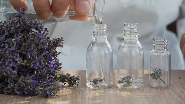 Close-up on the table are several bottles with lavender flowers, a man's hand pours alcohol into the bottles. Aromatherapy and production of natural organic perfumes.