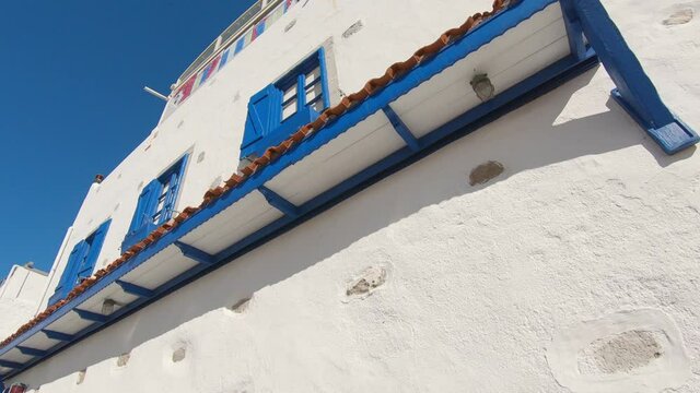 Low angle shot of popular aegean style building, white facade and blue window frame, summer vibe. 