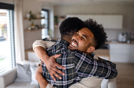Young happy adult brothers in kitchen indoors at home, hugging.