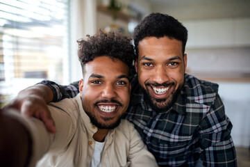 Portrait of young adult brothers in kitchen indoors at home, taking selfie.