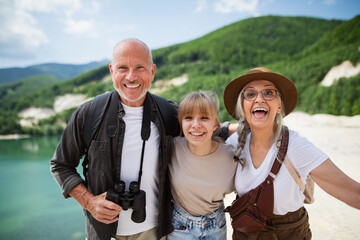 Happy preteen girl with grandparents on hiking trip on summer holiday, looking at camera.
