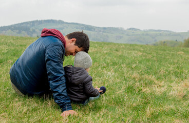 Naklejka na ściany i meble Father and son hugging on vacation on spring time meadow in mountains