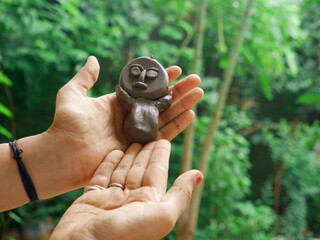 Girl hand holding soil made statue toy sculpture around green natural background.