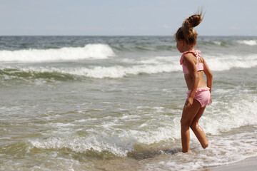 Little girl in a swimsuit splashes on the waves in the Baltic Sea.