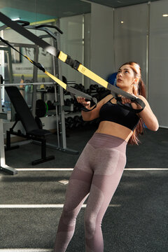 young caucasian woman working out with TRX inside the gym