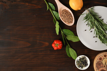 Assorted spices with fresh herbs on a wooden background. Natural food additives. Aromatic herbs and spices from garden, healthy cooking concept. Fresh lemon, tomato. Flat lay, top view