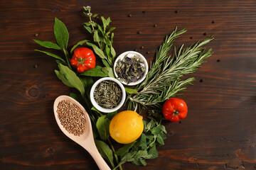 Assorted spices with fresh herbs on a wooden background. Natural food additives. Aromatic herbs and spices from garden, healthy cooking concept. Fresh lemon, tomato. Flat lay, top view
