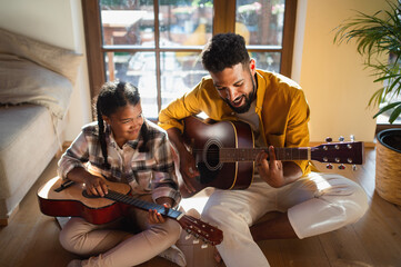 High-angle view of happy father with small daughter indoors at home, playing guitar.