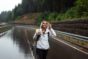 Young woman in raincoat standing on wet asphalt road and smiling