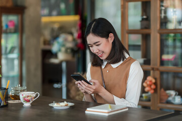 Image of young Asian woman relaxing at a café holding smartphone in happy.