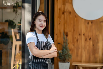 Asian woman small business owner wearing an apron stands in front of a café. Looking at camera.