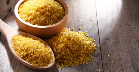 Composition with a bowl and spoon of uncooked bulgur on a table
